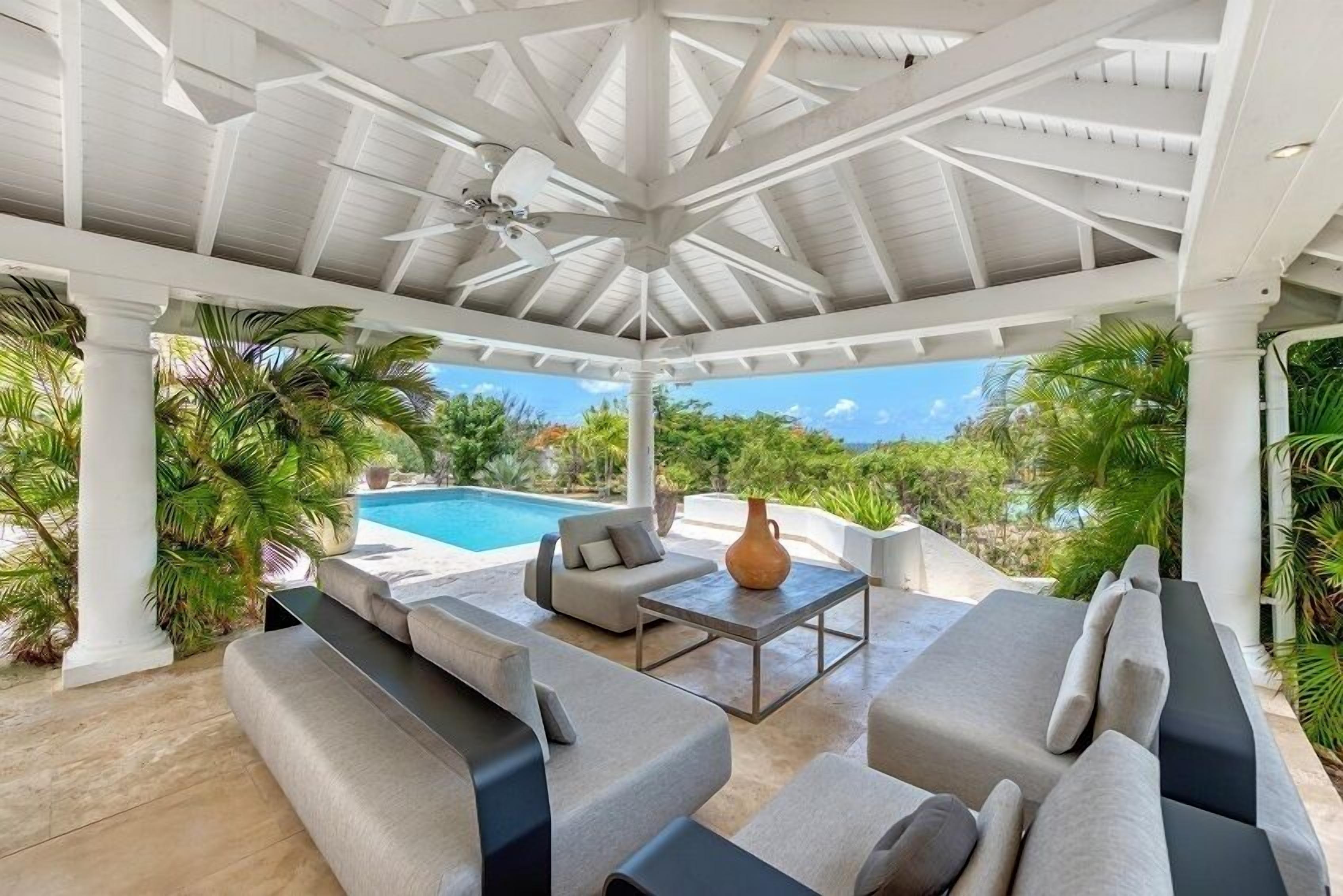 A covered outdoor seating area with a pool view, featuring sofas and a table.