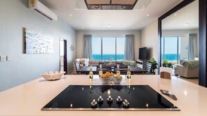 Un salon moderne doté d’un îlot central, d’un ensemble de canapés, d’un téléviseur et offrant une vue sur la mer.