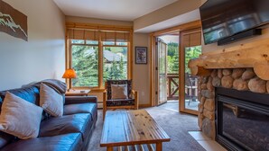 A cozy living room with a sofa, a wooden coffee table, a fireplace, and a television mounted above it. - Beautiful one bedroom condo steps from the American Flyer Lift. (Copper Mountain)