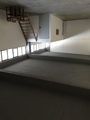 An empty room with a wooden ladder, a small window, and a door. - Factory style residence (Ilion)