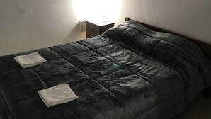 Un lit simple avec une couverture sombre et deux serviettes blanches pliées.