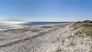A beach with a wooden boardwalk leading to a pier.