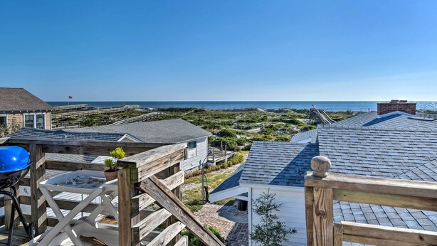 A coastal property with a wooden deck, a barbecue grill, and a view of the ocean.