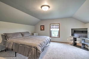 A bedroom with a bed, a nightstand, a TV on a stand, and a window with curtains.