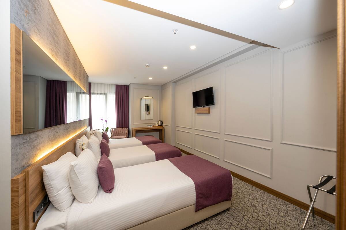 A hotel room with two beds, a TV mounted on the wall, a mirror, and a small table with a lamp.