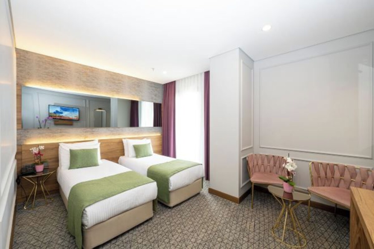 Une chambre d’hôtel avec deux lits, un coin salon avec une table et un téléviseur fixé au mur.