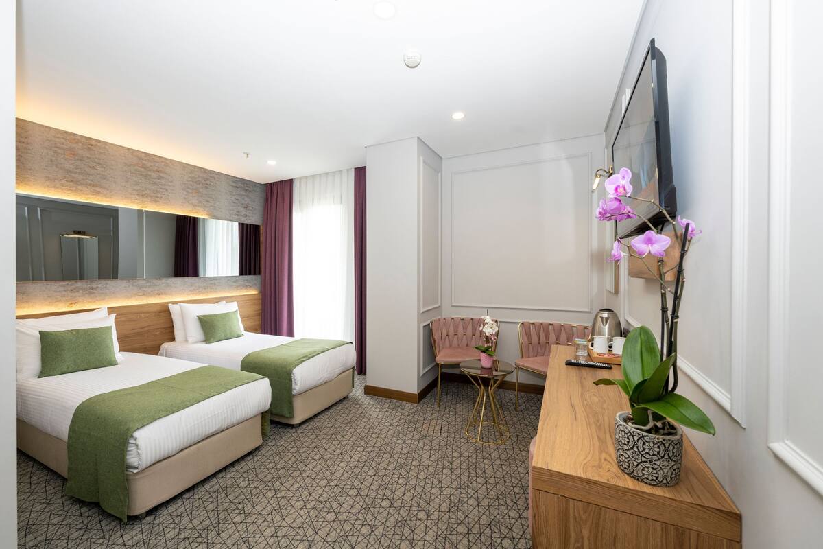 A hotel room with two beds, a desk with a chair, a TV, and a potted plant.