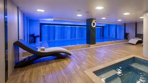 Un espace piscine intérieur moderne, doté d’un plancher en bois, d’une chaise longue et d’un petit bassin.