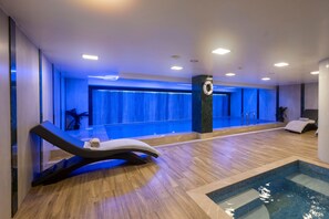 Un área de piscina interior moderna con suelo de madera, una tumbona y una piscina pequeña.
