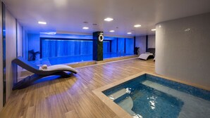 A modern indoor swimming pool area with a wooden floor, a lounge chair, and a view of the pool. - Graziella Gold Hotel (Istanbul)