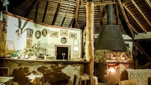 A rustic interior with a stone fireplace, wooden beams, and a bar area with various items. - Antucalhue (Antuco)