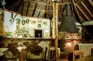 Un interior rústico con chimenea de piedra, vigas de madera y una zona de bar con diversos objetos.