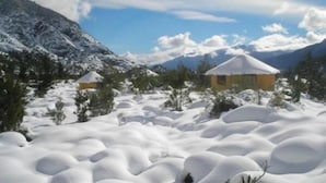 A snowy landscape with two yellow buildings surrounded by snow-covered trees and mountains in the background. - Antucalhue (Antuco)