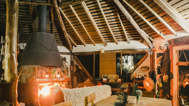 A rustic interior with a stone fireplace, wooden beams, and a dining area with a table and chairs. - Antucalhue (Antuco)