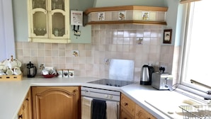 A kitchen with wooden cabinets, a stove, a sink, and a window. - 14 Tweed Cottage (Jedburgh)