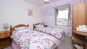 A bedroom with two single beds, a wooden wardrobe, a window with a view, and a bedside table with a lamp. - 14 Tweed Cottage (Jedburgh)