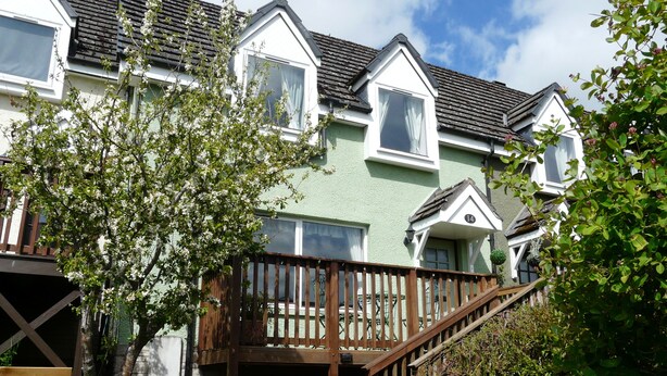 A row of houses with a wooden deck and stairs leading to the entrance. - 14 Tweed Cottage (Jedburgh)