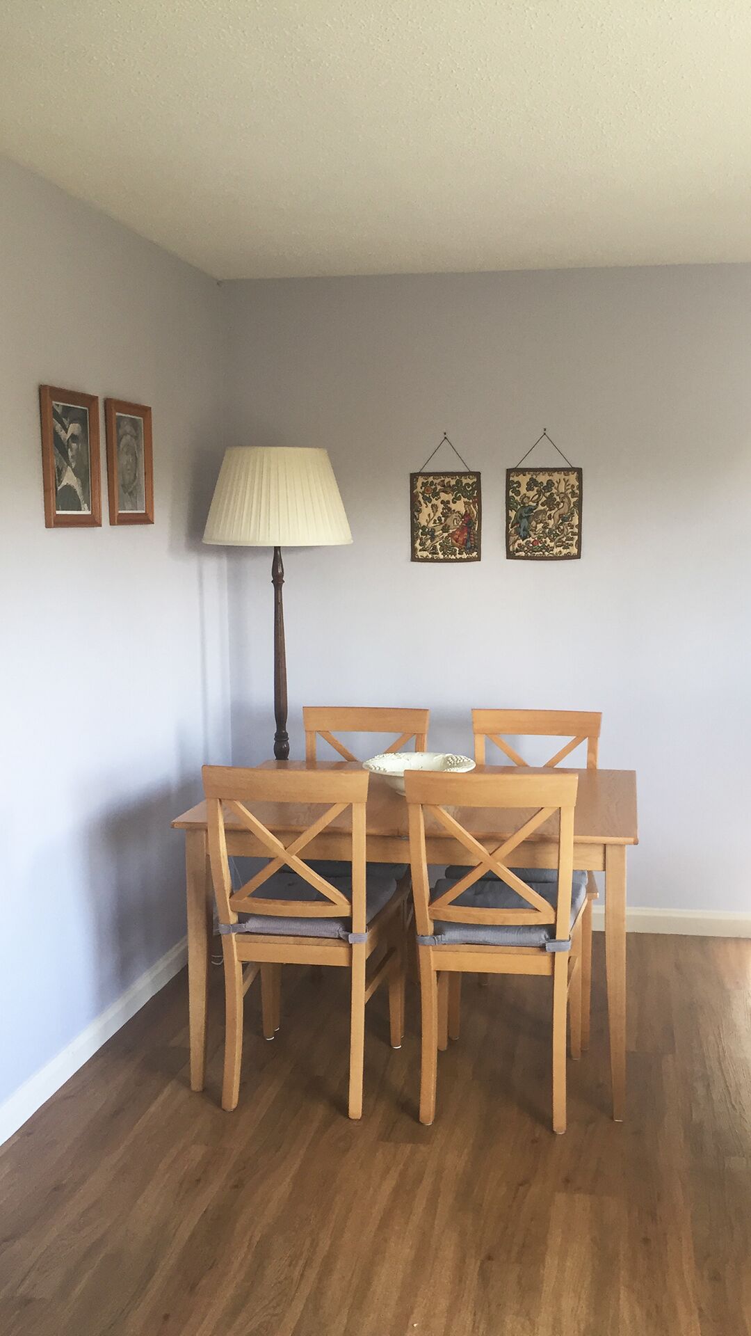 A dining area with a wooden table and chairs, a lamp, and two framed pictures on the wall.