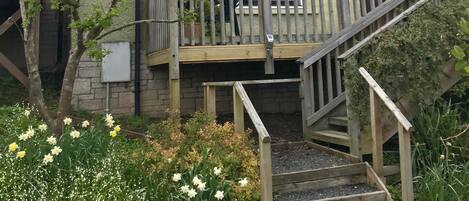 A two-story house with a balcony, a staircase, and a garden with flowers.