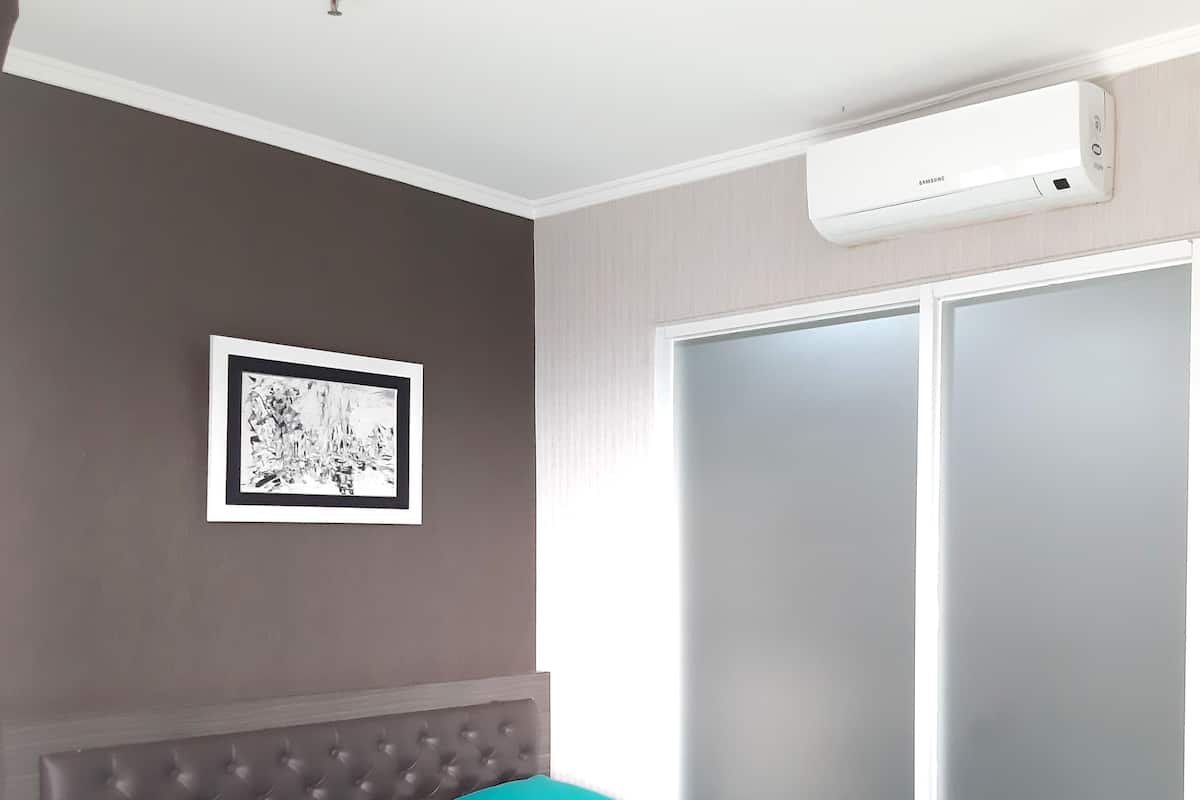 A bedroom with a bed, a framed picture on the wall, and an air conditioning unit.