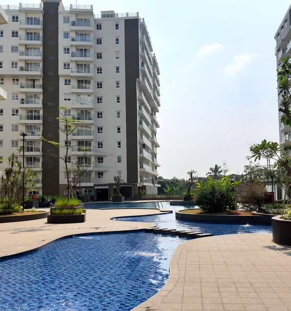 A residential building with multiple balconies and a swimming pool area with tiled flooring and planters. - High Livin Apartment Pasteur (Cimahi)