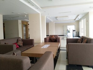 A modern hotel lobby with sofas, a wooden table, and a view of the kitchen area. - High Livin Apartment Pasteur (Cimahi)