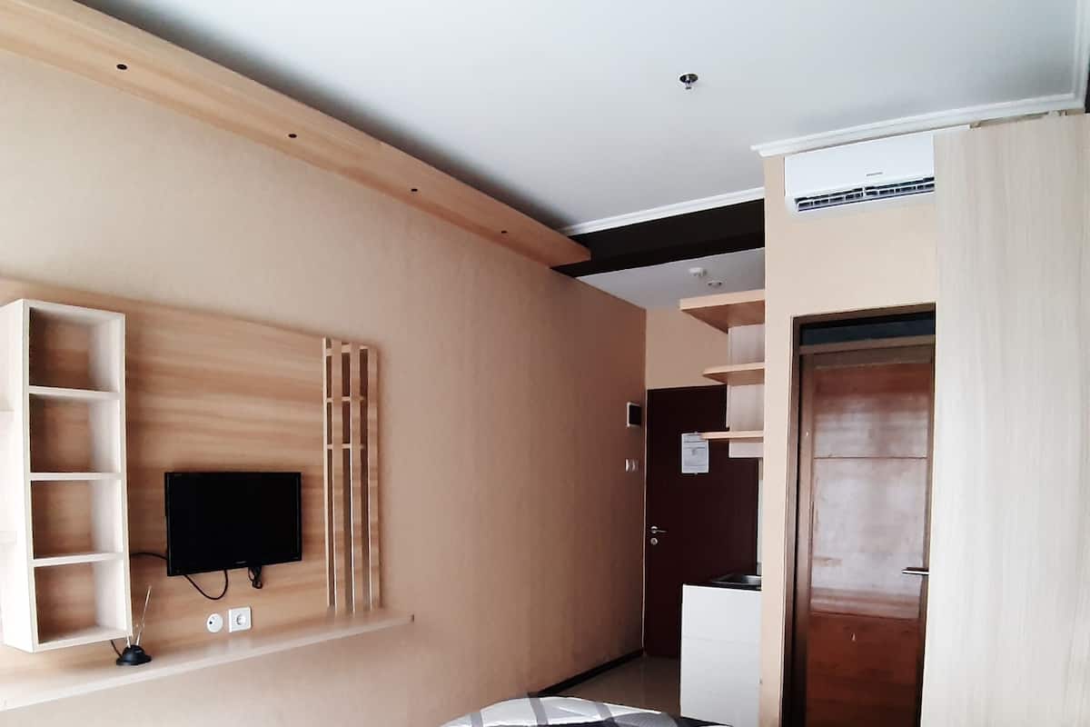 A hotel room with a bed, a TV mounted on the wall, a wardrobe, and a kitchenette.