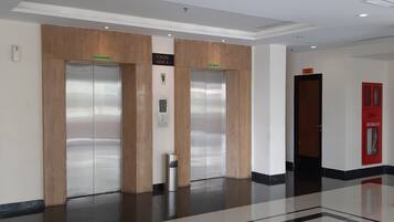 A clean, modern lobby with two elevators, a fire hydrant, and a polished floor.
