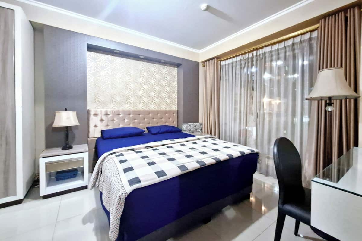 A hotel room with a large bed, a bedside table with a lamp, a chair, and a desk with a lamp.