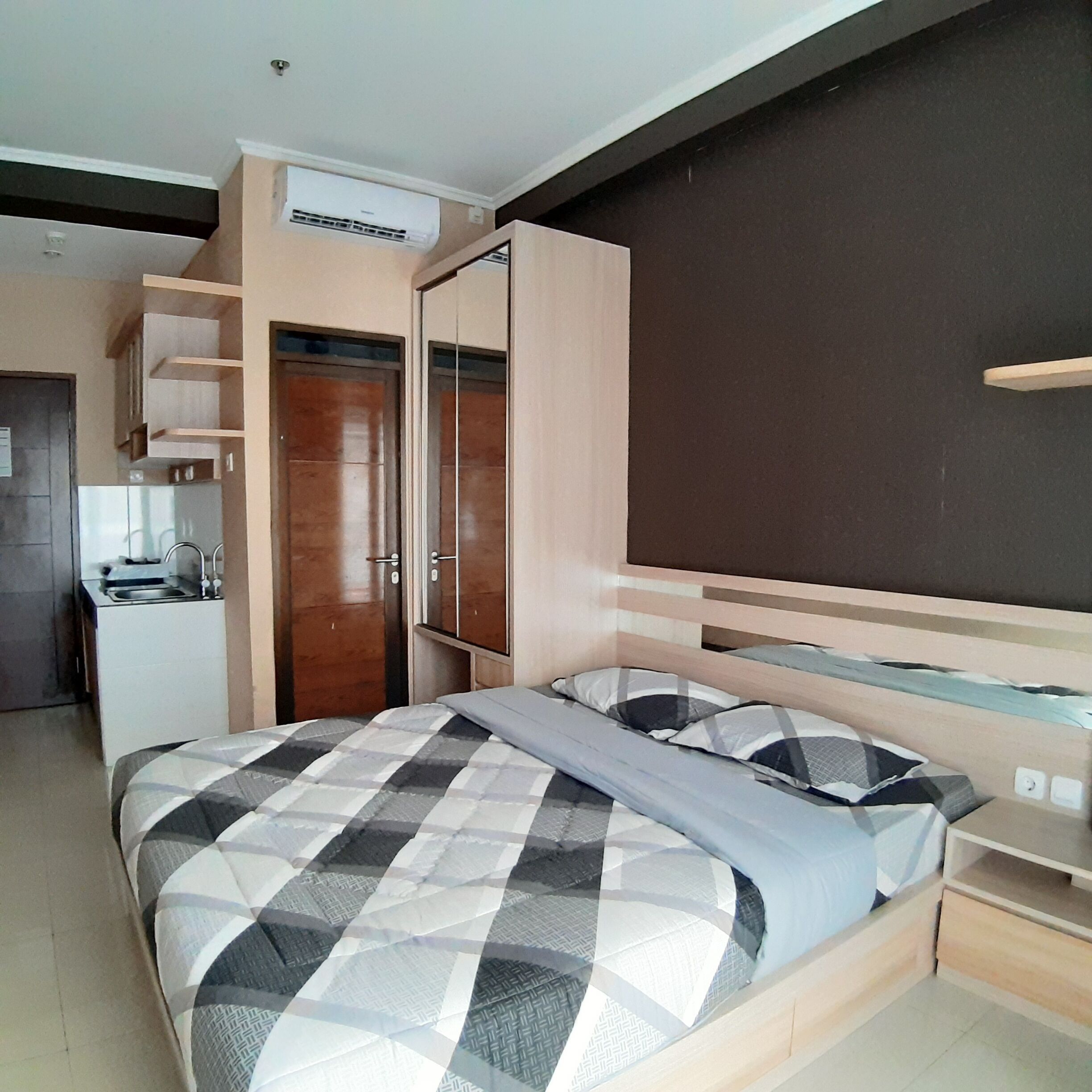 A bedroom with a bed, a wardrobe, a desk, and an air conditioning unit.
