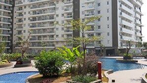 Un moderno edificio de apartamentos con varios balcones y un área de piscina con jardines ajardinados.