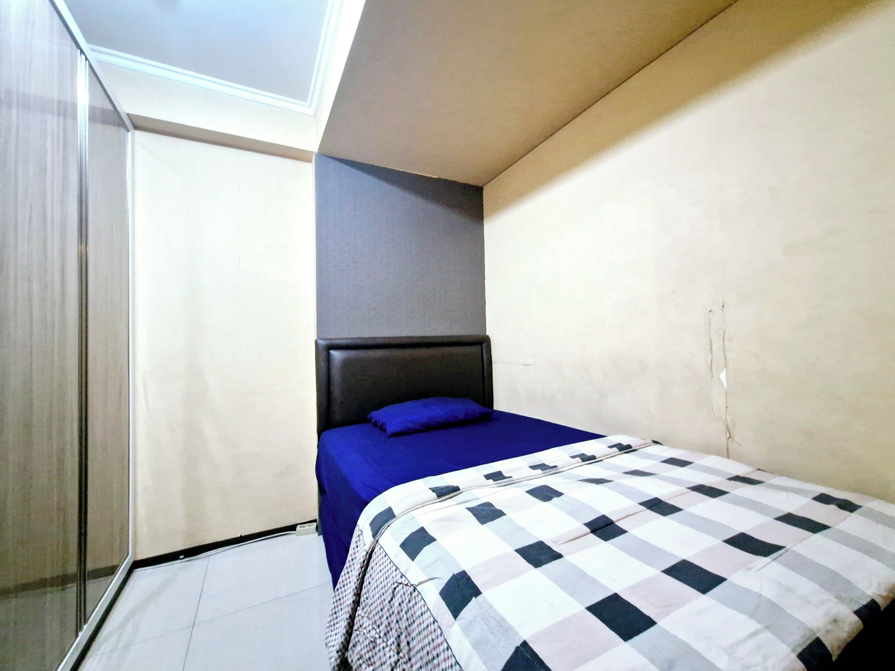 Une petite pièce, de taille modeste, comprenant un lit simple, une tête de lit grise et une couvre-lit bleue.