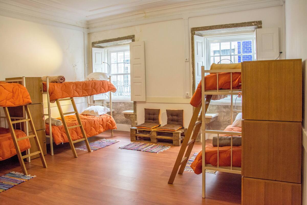 A dormitory room with bunk beds, a small table, and a window with a view.