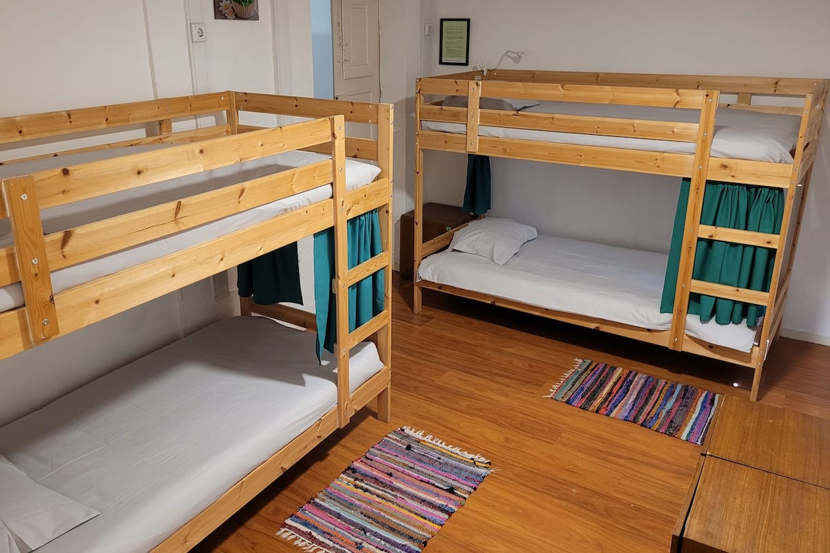 Two bunk beds in a room with wooden flooring, a colorful rug, and a door in the background.
