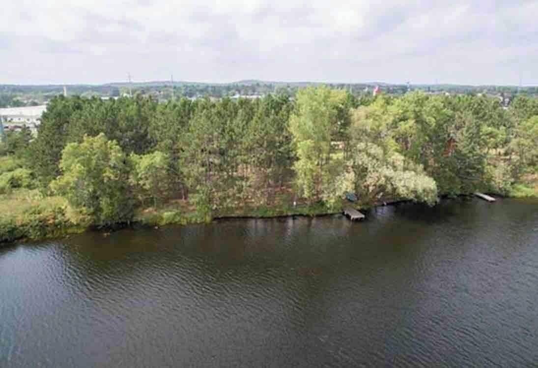 Une rivière bordée d’une forêt dense d’un côté et offrant, de l’autre, une vue lointaine sur un paysage urbain.