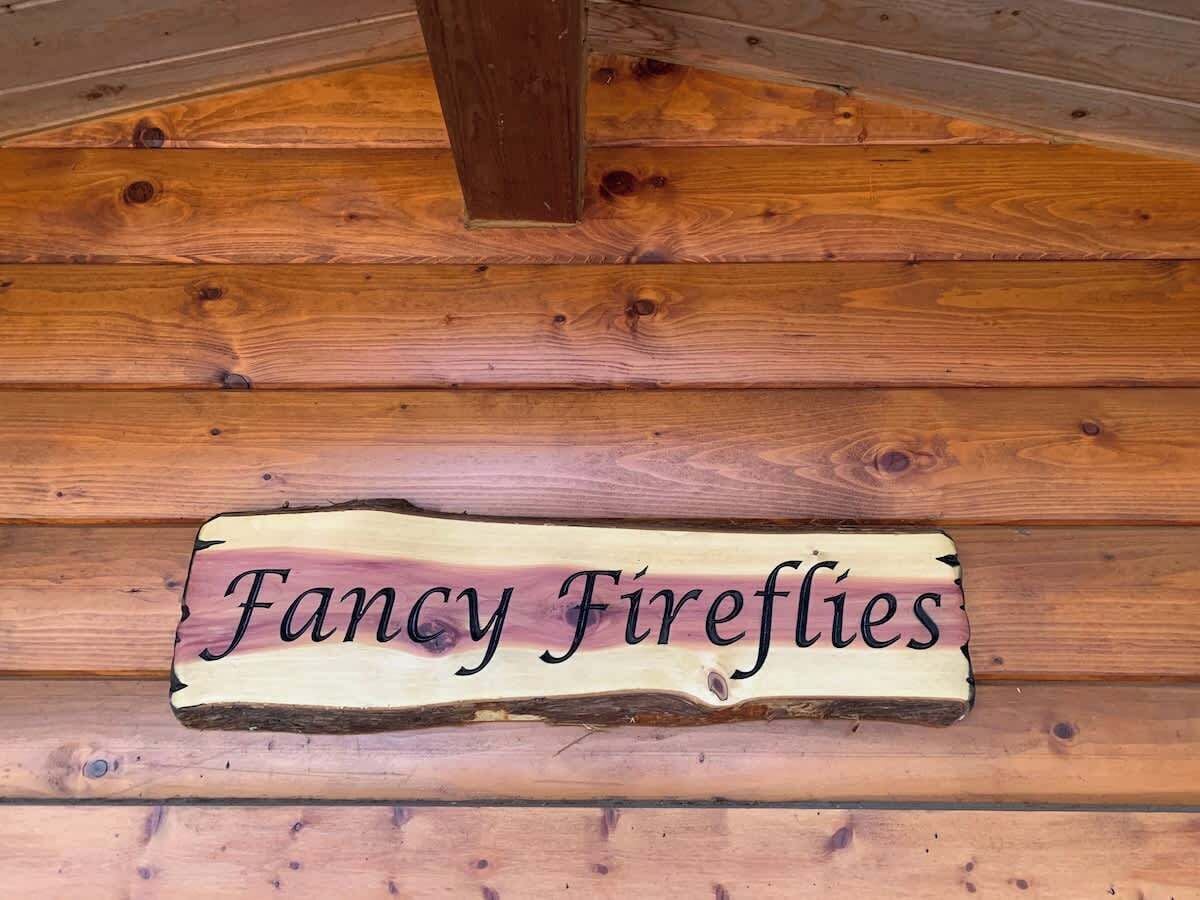 A wooden sign with the text "Fancy Fireflies" on a log wall.