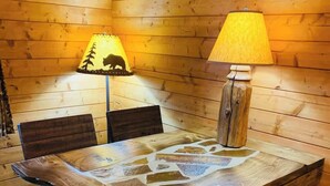 Ein Holzinnenraum mit einem Tisch, der eine einzigartige Mosaikplatte hat, zwei Stühlen, einer Lampe und einer kleinen Küchenzeile mit einem Herd.