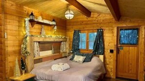 Ein gemütliches Schlafzimmer in einer Blockhütte, mit einem Bett, einem kleinen Tisch und einem Fenster mit Vorhängen.