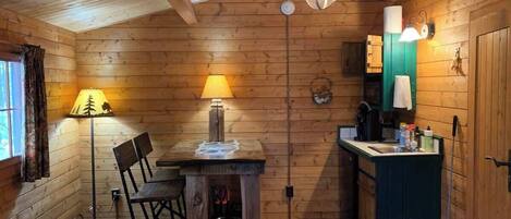 Een gezellig houten interieur met een eettafel, stoelen, een klein keukentje met een spoelbak en een afvalbak.