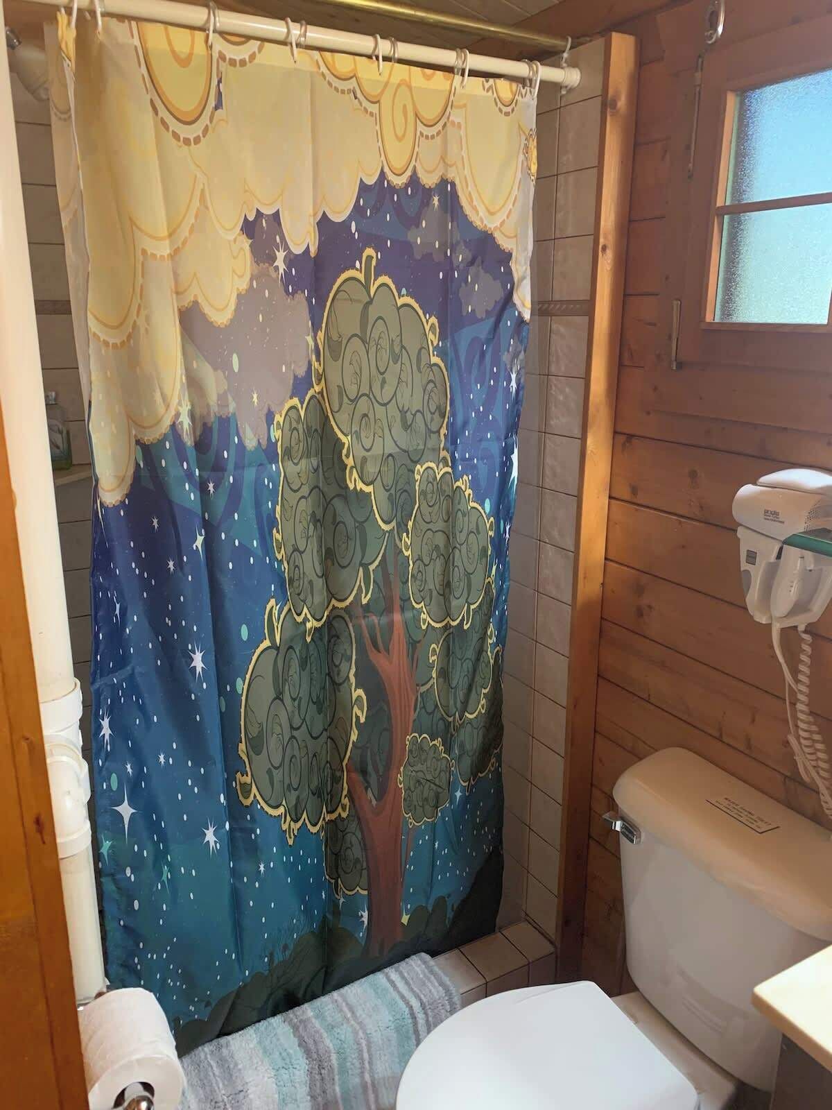 Un baño con cortina de ducha decorada con un diseño de árbol, un inodoro y una ventana.