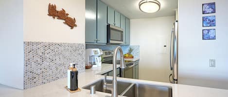 A modern kitchen with a stainless steel sink, blue cabinets, a microwave, and a coffee maker.