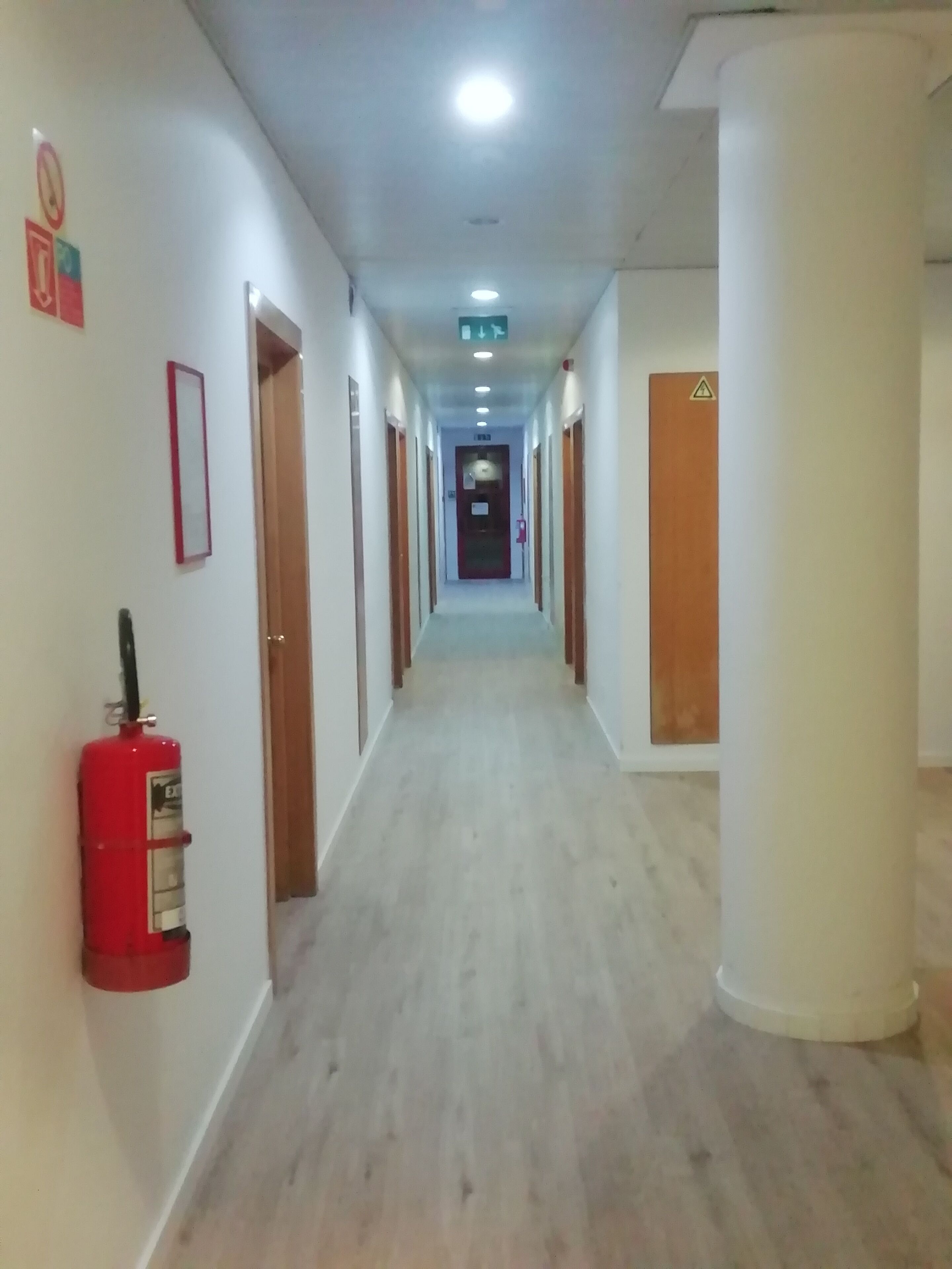 A long, narrow hallway with doors on both sides, a fire extinguisher mounted on the wall, and a ceiling light.