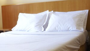 A bed with white bedding and pillows, a wooden headboard, and a wooden nightstand.