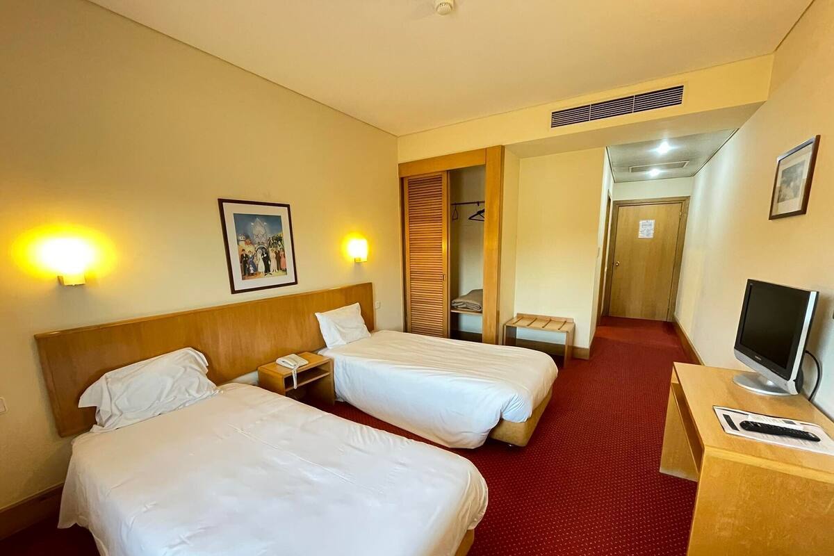 Une chambre d’hôtel avec deux lits, un bureau avec un ordinateur et une télévision.
