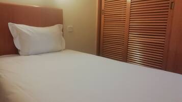 A hotel room with a neatly made bed, a wooden headboard, and a wooden wardrobe with horizontal slats.