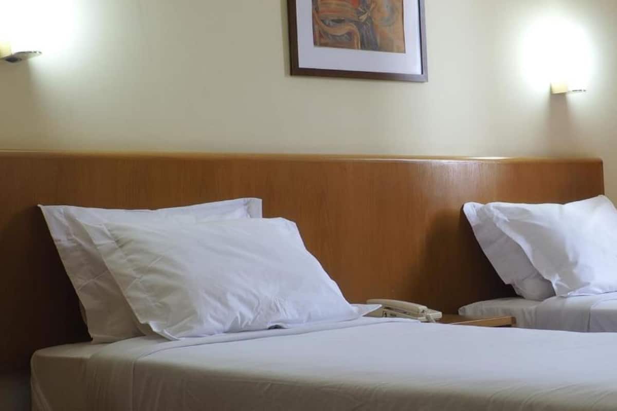 Une chambre d’hôtel avec deux lits, chacun doté de draps et d’oreillers blancs. On y trouve une tête de lit en bois, une œuvre d’art encadrée au mur et une table de chevet avec un téléphone.