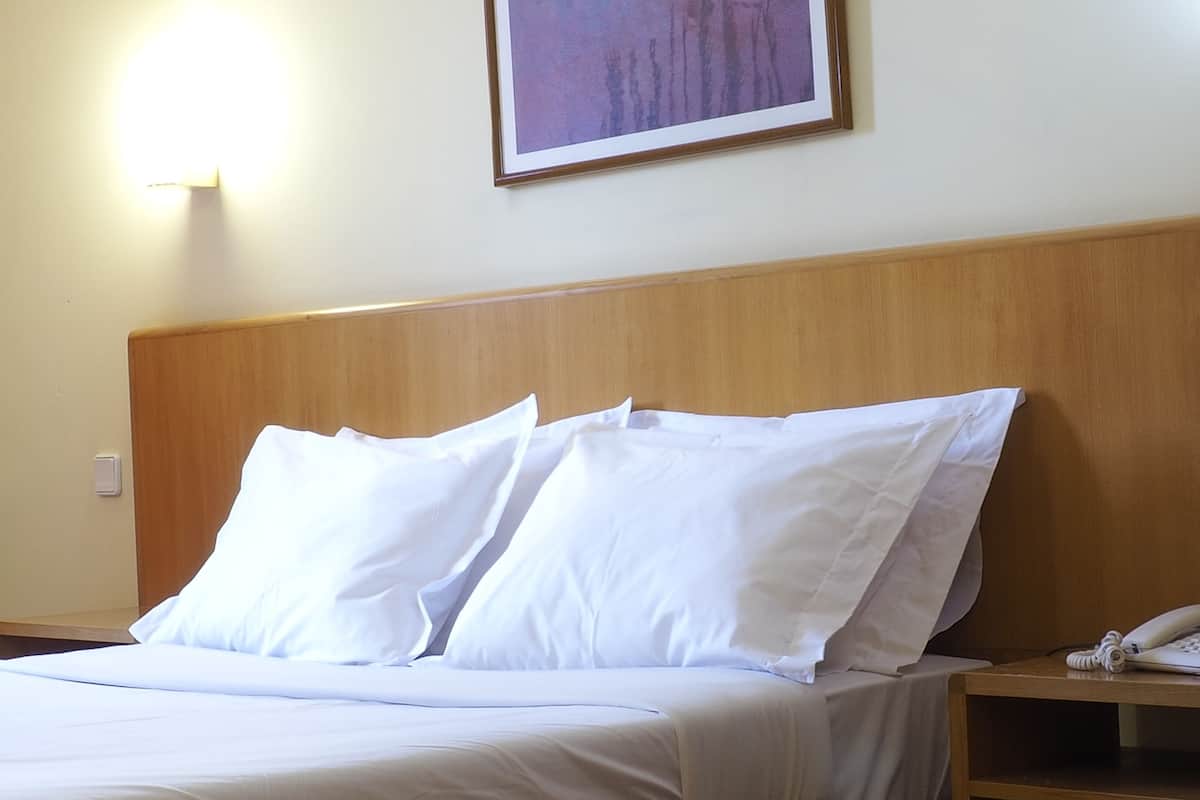 Une chambre d’hôtel avec une tête de lit en bois, du linge de lit blanc et une table de chevet avec un téléphone.