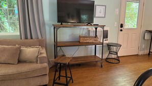 A living room with a sofa, a TV on a wooden stand, a small table, and a door with a window. - Charming Orchard Cottage…Pet Friendly!! (Chico)