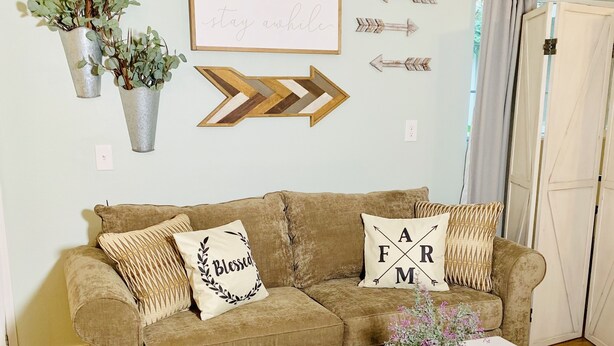 A living room with a brown sofa, two pillows with text, a white coffee table, and decorative plants. - Charming Orchard Cottage…Pet Friendly!! (Chico)