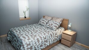 Un dormitorio con cama, mesita de noche, lámpara, ventana y una planta en maceta.